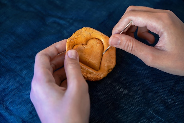 Handen close-up kras bruine suiker karamel snoep koekjes met een metalen naald in de vorm van een hart...