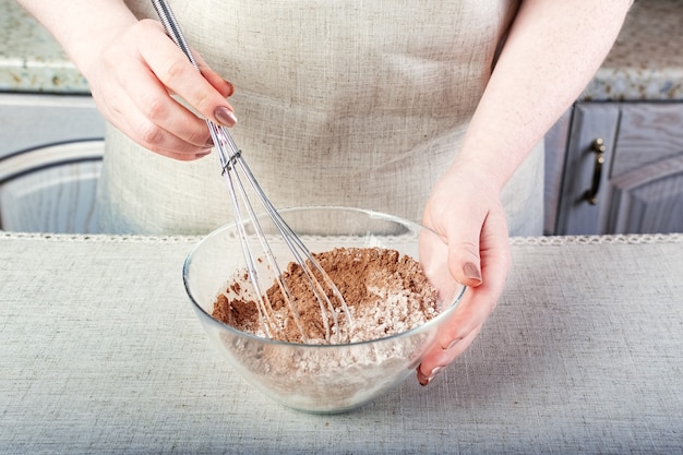 Handen die cacaopoeder en bloem mengen met een garde