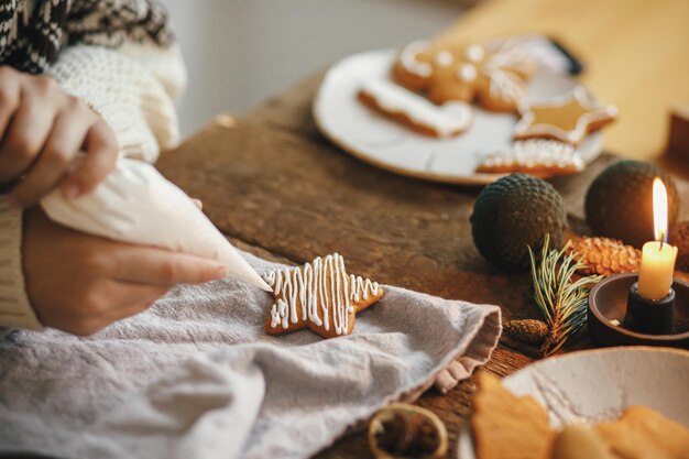 Handen die de ster van het de peperkoekkoekje van Kerstmis verfraaien met suikerglazuur op rustieke lijst Atmosferisch beeld