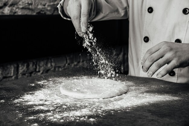 Handen die een pizzadeeg maken met bloem op het grijze betonnen oppervlak