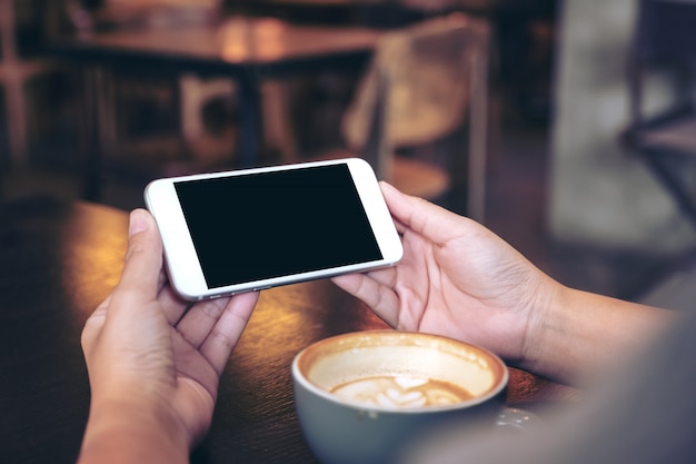 Handen die een witte mobiele telefoon met leeg zwart scherm houden en gebruiken