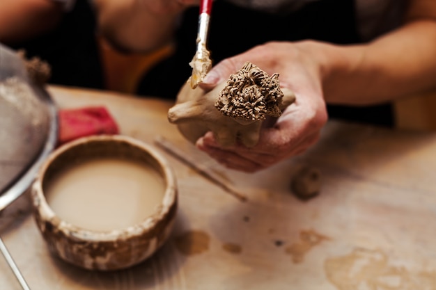 Handen die en beeldhouwwerk met klei werken beëindigen op houten lijst in workshop