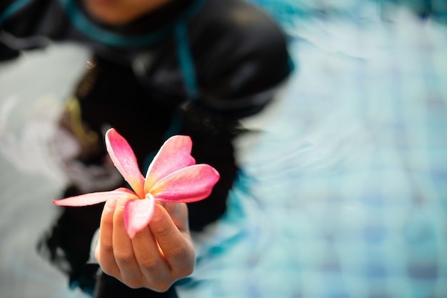 Foto handen die frangipanibloemen met blauw water in het zwembad houden