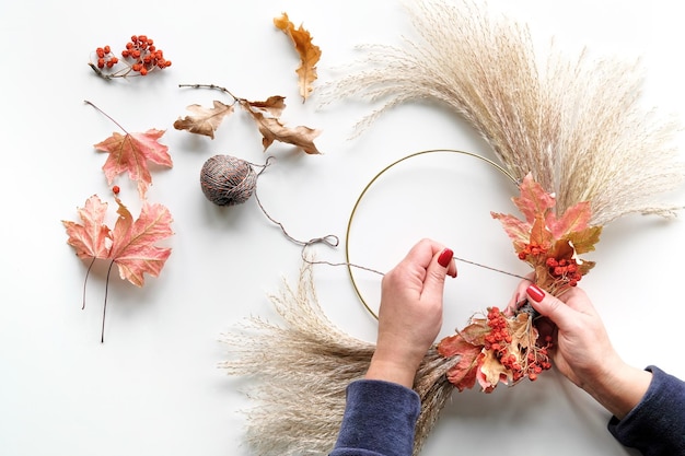 Handen die gedroogde bloemenkrans maken van droog pampagras en herfstbladeren Handen in trui stropdas decoraties aan metalen frame