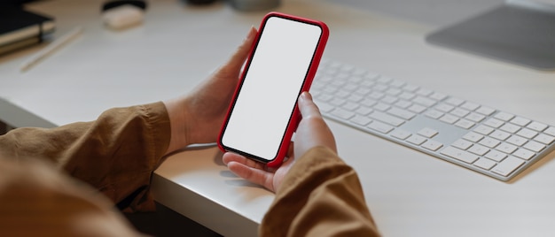 Handen die lege het schermsmartphone op wit bureau met computerapparaat houden