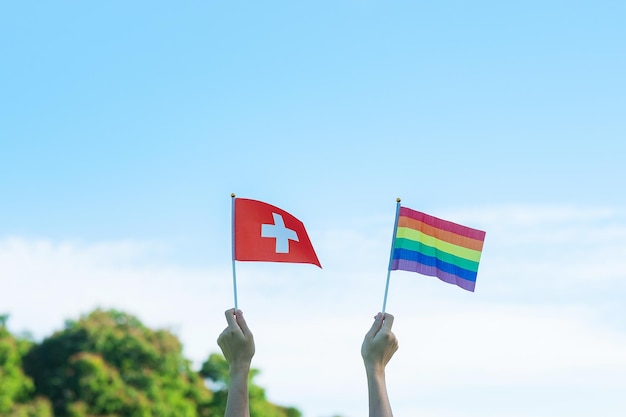 Handen die Lgbtq-regenboog en de vlag van Zwitserland tonen op de achtergrond van de natuur Ondersteuning voor lesbische homo-biseksuele transgender en queer-gemeenschap en Pride-maandconcept