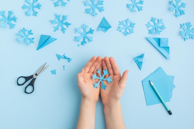 Foto handen die papieren sneeuwvlokken maken op blauwe kinderhanden foto van hoge kwaliteit