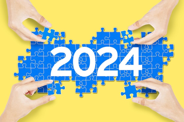 Handen die samenwerken om 2024 nieuwe jaarnummers op gele achtergrond te construeren