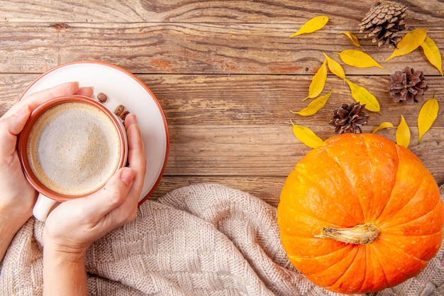 Handen die warme koffie op houten achtergrond met pompoen houden