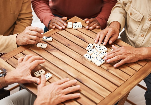 Handen dominostenen en vrienden in bordspellen op houten tafel voor leuke activiteit sociale binding of verzamelen Hand van dominospelers met rechthoekige nummerblokken die in groep spelen voor amusement