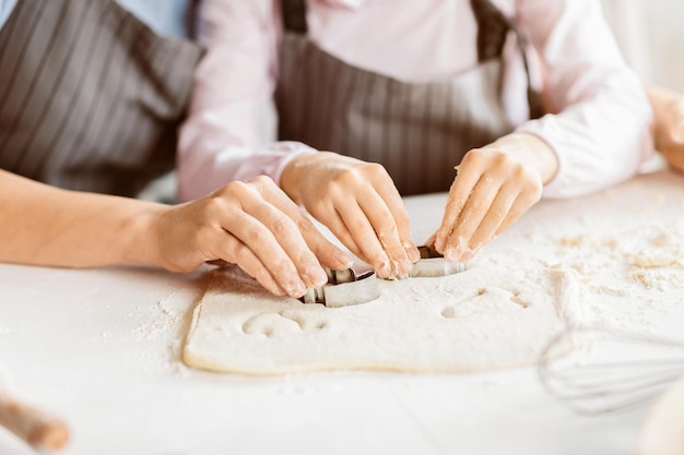 Handen gebruiken koekjessnijders op het deeg om vormen te maken