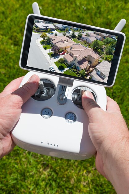 Handen houden drone quadcopter controller met residentiële huizen op het scherm