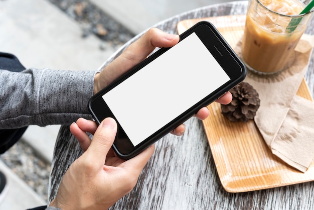 Handen houden en het gebruik van mobiele telefoon met een leeg scherm op houten tafel in café.