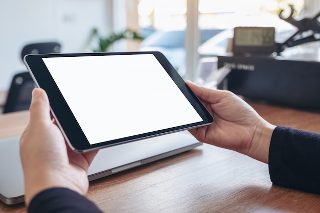 handen houden en met behulp van zwarte tablet-pc met lege witte desktop-scherm met notebook op houten tafel in kantoor