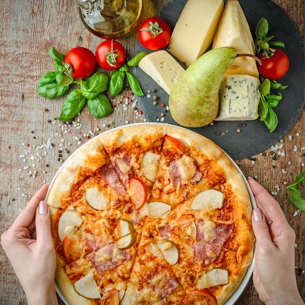 Handen houden Hawaiiaanse pizza op een houten tafel