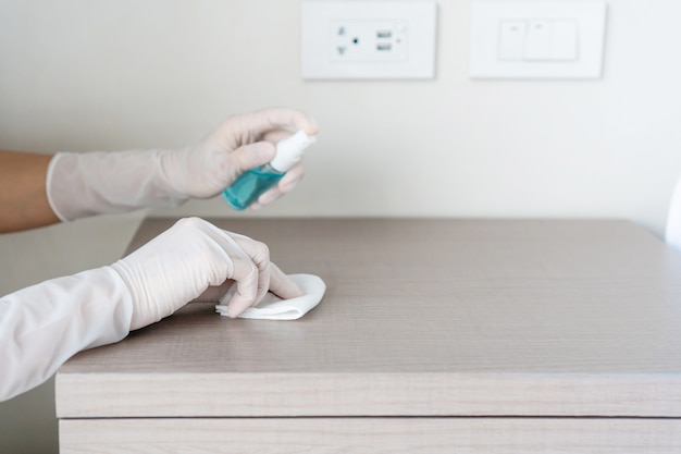 Foto handen in beschermende handschoen met nat afveegdoekje en alcoholspray afvegen kast tegen stof en ziektekiemen