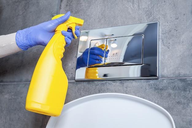 Handen in beschermende handschoenen die de knop voor het doorspoelen van het toilet schoonmaken