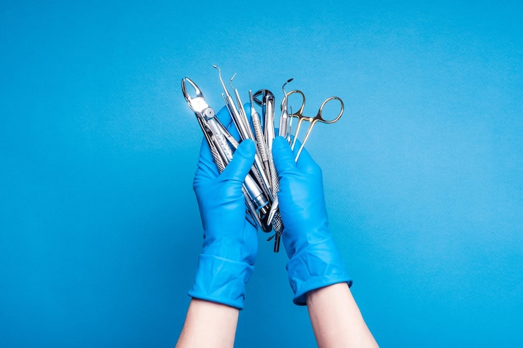 Foto handen in blauwe handschoenen met tandheelkundige apparatuur en metalen instrumenten op blauwe achtergrond