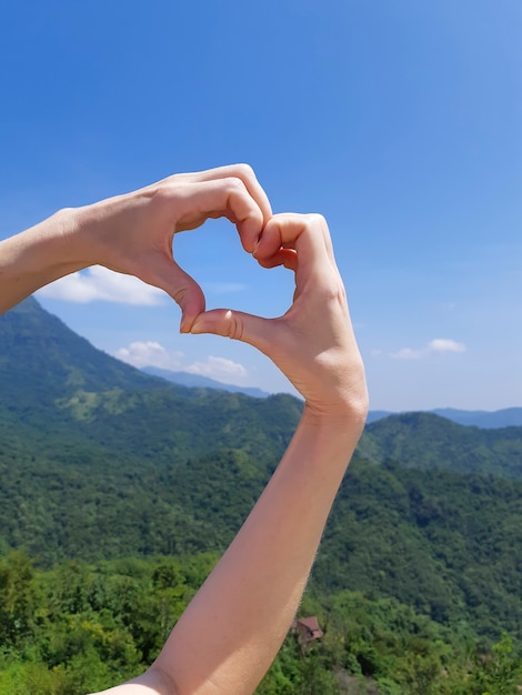 Handen in de vorm van hartvorm tegen blauwe lucht en bergen. Milieu dag concept.