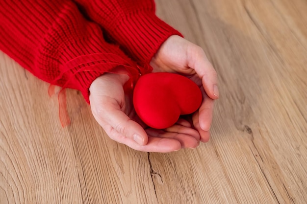 Handen in een rode trui met een rood hart met linten