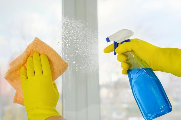 Handen in een rubberen beschermende handschoen wassen de ramen met reinigingsmiddel