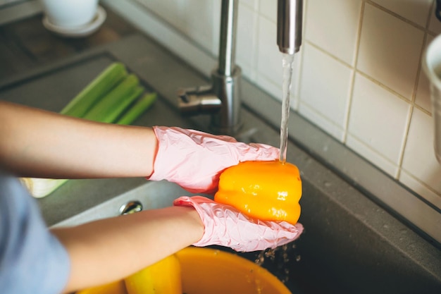 Handen in handschoenen met peper groenten wassen tijdens virusepidemie Vrouw in roze handen wassen van verse groenten bereiden voor het koken maaltijd in moderne keuken