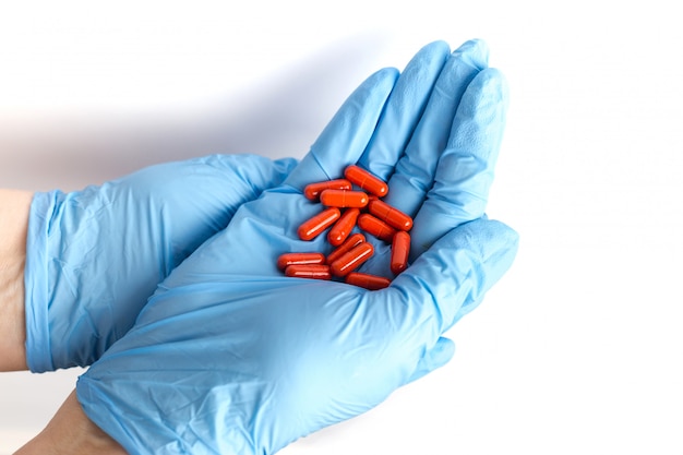 Foto handen in medische handschoenen houden een handvol rode pillen. blauwe wegwerphandschoenen geïsoleerd. farmaceutisch concept. het medicijn