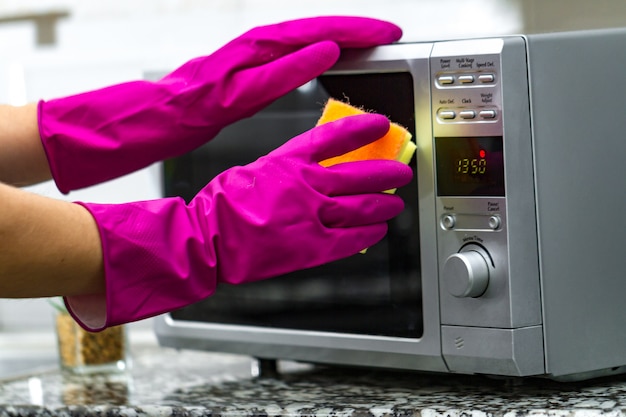 handen in rubberen handschoenen schoonmaken van een magnetron met behulp van een spons