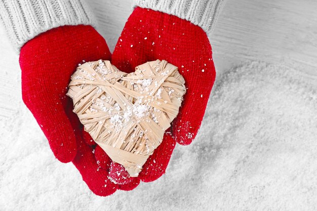 Handen in warme rode handschoenen met rieten hart op besneeuwde achtergrond