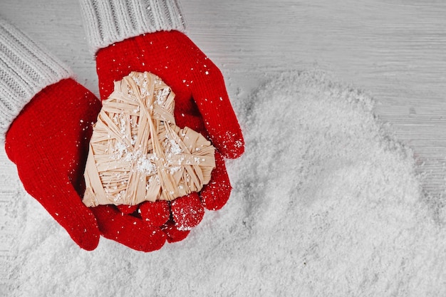 Handen in warme rode handschoenen met rieten hart op besneeuwde achtergrond