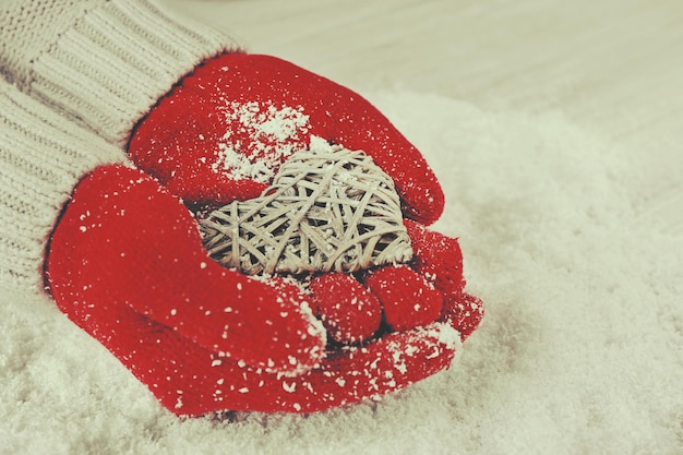 Handen in warme rode handschoenen met rieten hart op besneeuwde achtergrond