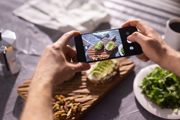 Handen maken op de smartphone foto's van twee mooie sandwiches met gezonde zure room en avocado