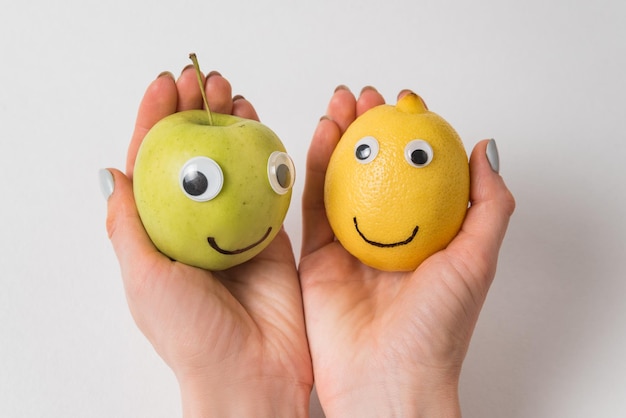 Handen met appel en citroen met grappige gezichten op witte achtergrond