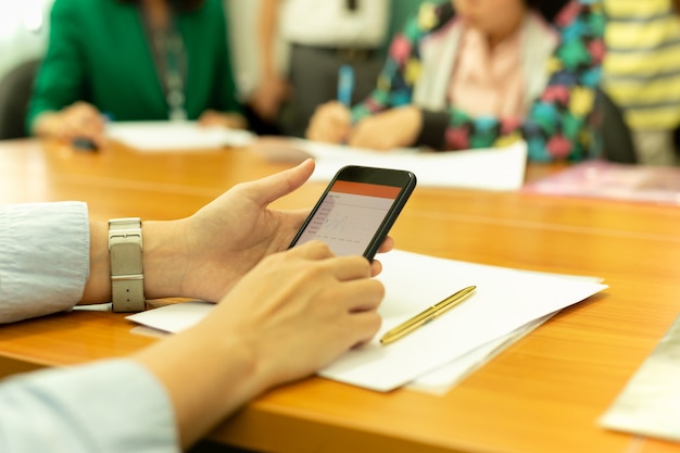 Handen met behulp van mobiele telefoon met de grafiek van het voorraadgeld met groep bedrijfsmensen.