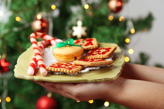 Handen met bord met zelfgemaakte koekjes en snoepjes, op lichte achtergrond