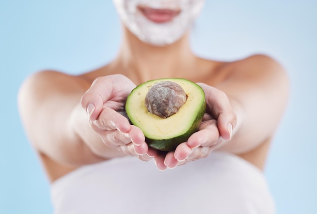 Handen met een avocadofruit voor huidverzorging, schoonheid en cosmetische wellness op een blauwe mockupstudio-achtergrond Vrouw met gezichtsmasker voor gezondheid, huid- en lichaamsverzorging die voeding geeft om te eten