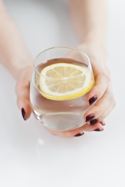 Handen met een glas helder water met citroen.