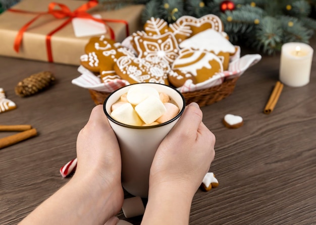 Handen met een kopje cacao met marshmallows Kerstkaart met ruimte voor tekst op een donkere achtergrond met een geschenkdoos met dennentakken, peperkoeklollies en kaneelstokjes