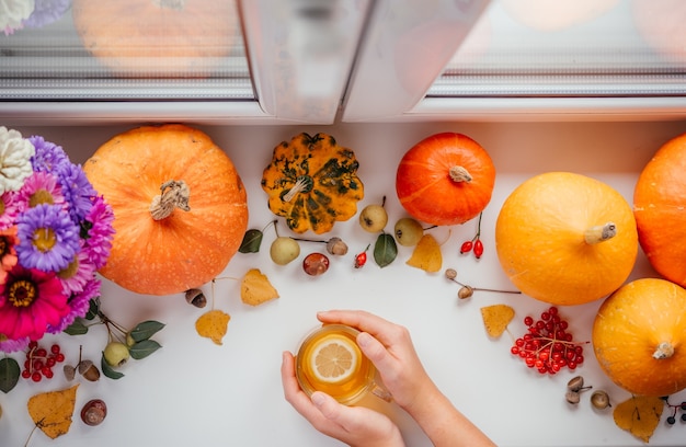 Handen met een kopje citroenthee over de achtergrond van de herfstpompoen