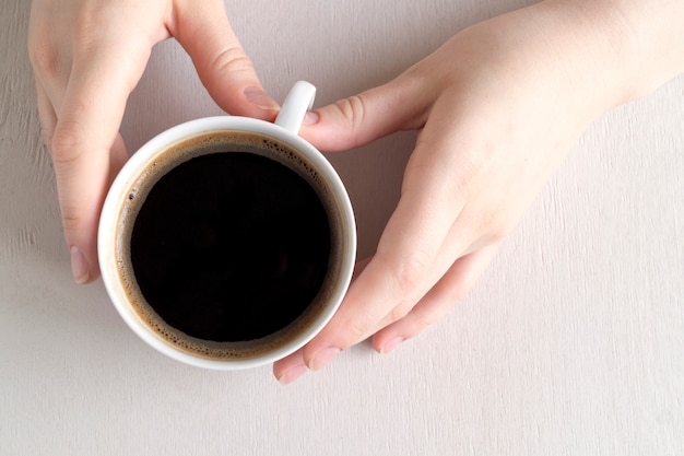 Handen met een kopje koffie op een lichte tafel.