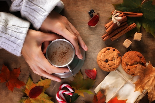 Handen met een mok hete koffie op een tafel met herfstbladeren