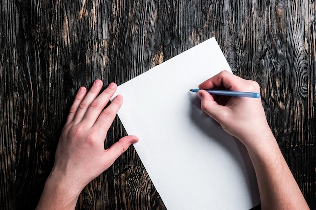 Foto handen met een papieren vel en een pen op een donkere houten tafel