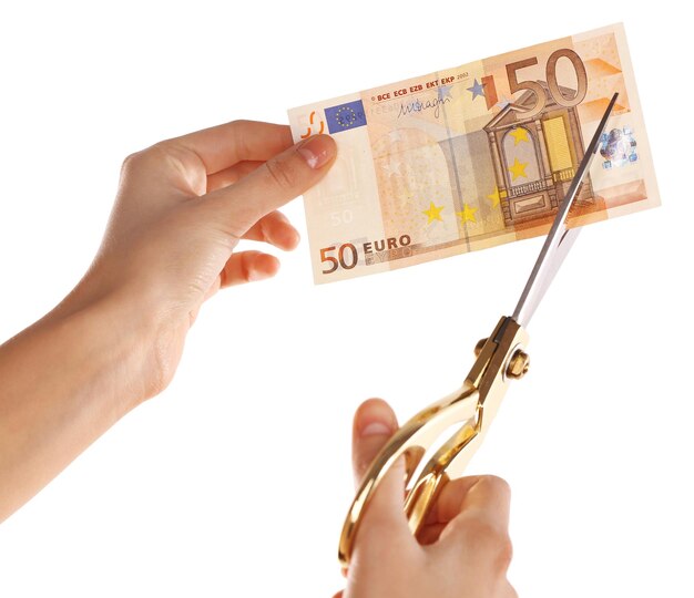 Handen met een schaar die eurobankbiljetten snijden die op wit worden geïsoleerd