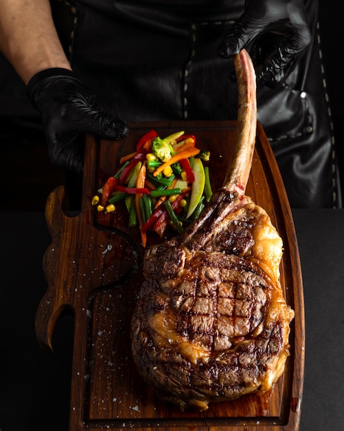 Handen met gekookte Tomahawk (long bone ribeye) steak op een serveerplank. Rustige afbeelding, verticale oriëntatie