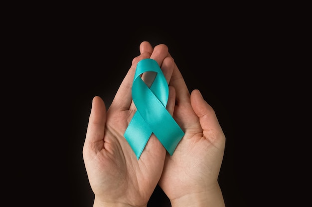 Foto handen met groenblauw lint symbolisch voor baarmoederhalskanker, eierstokkanker, gynaecologische kanker en pcos
