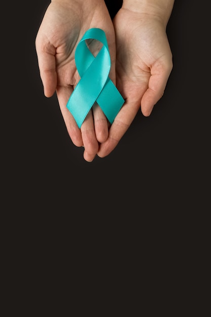 Foto handen met groenblauw lint symbolisch voor baarmoederhalskanker, eierstokkanker, gynaecologische kanker en pcos