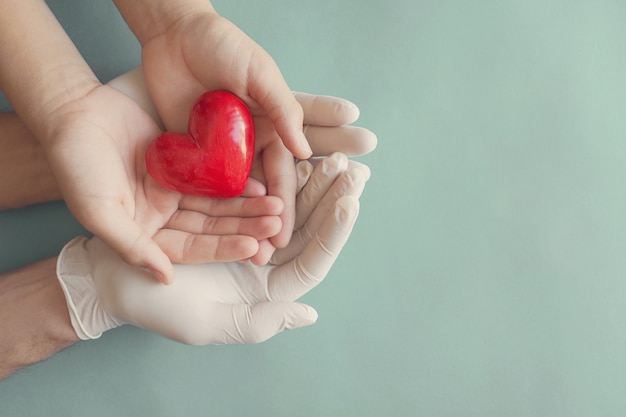 Foto handen met handschoenen die kindhanden en rood hart, ziektekostenverzekering en schenkingconcept houden