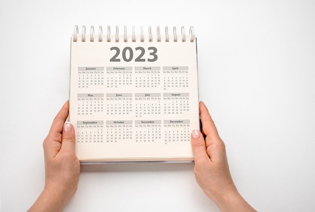 Handen met kalender voor 2023 op witte achtergrond Resolutie strategie oplossing doel zaken en Nieuwjaar vakantie concepten