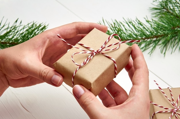 Handen met kerst geschenkdoos over witte tafel met pijnboomtakken