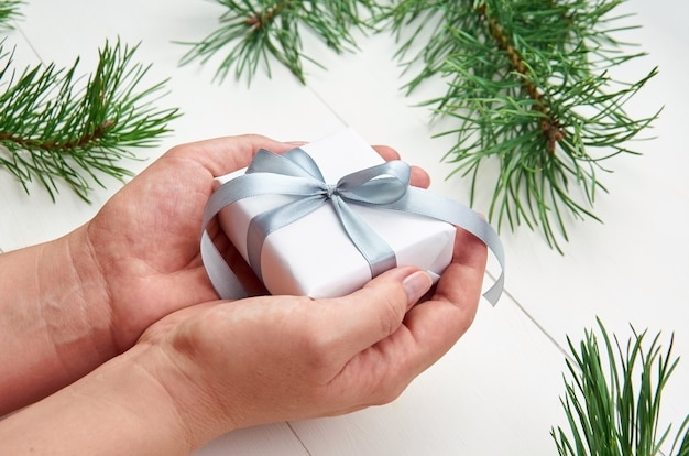 Handen met kerstcadeaudoos over witte tafel met pijnboomtakken